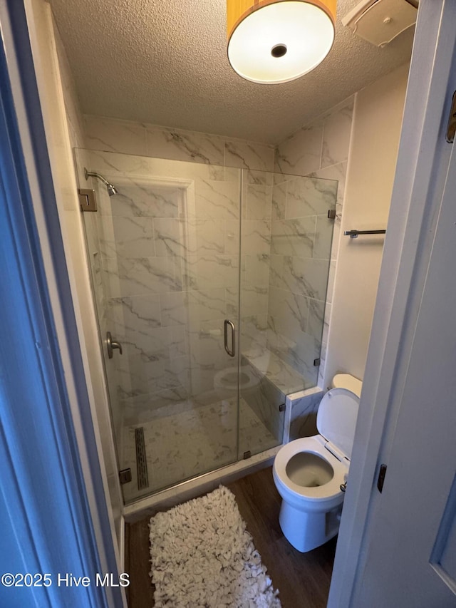 full bathroom with a stall shower, a textured ceiling, toilet, and wood finished floors