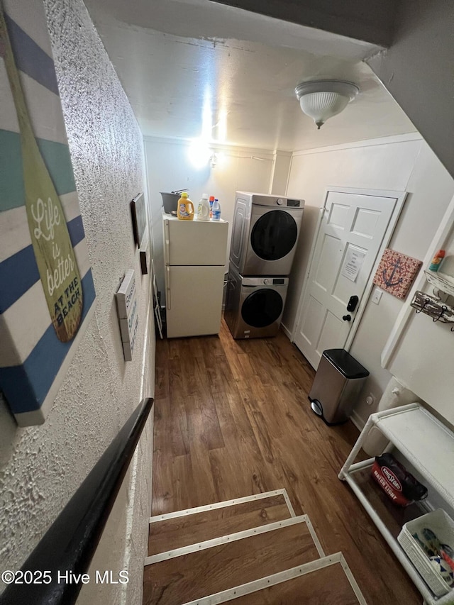 clothes washing area featuring laundry area, stacked washing maching and dryer, and wood finished floors