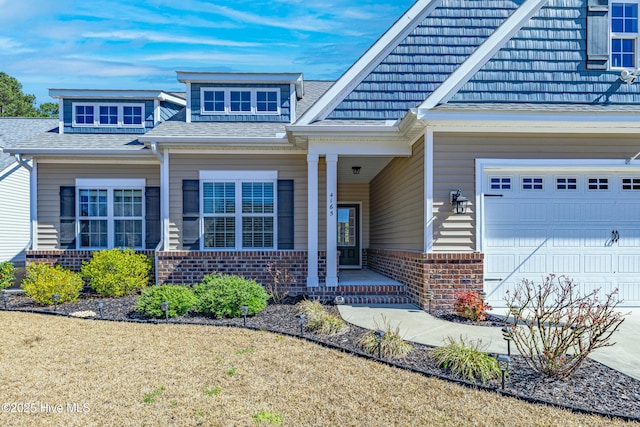 view of exterior entry featuring brick siding, covered porch, and a shingled roof