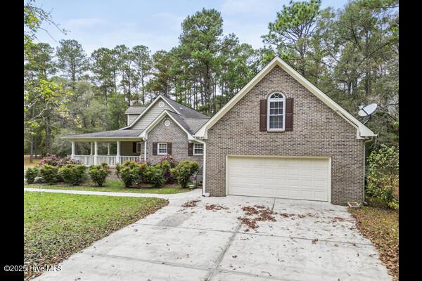 view of front facade with a porch, an attached garage, brick siding, concrete driveway, and a front lawn