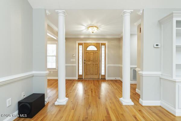 entrance foyer featuring ornate columns, crown molding, baseboards, and light wood-style floors