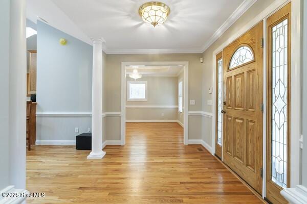 foyer featuring light wood finished floors, decorative columns, and crown molding