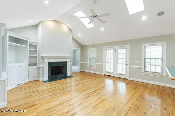 unfurnished living room with a skylight, light wood-style flooring, ceiling fan, and a high end fireplace