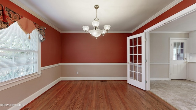 unfurnished room featuring a notable chandelier, crown molding, wood finished floors, and baseboards