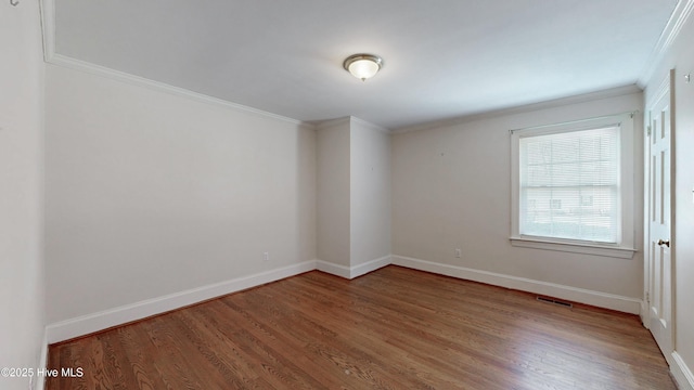 empty room featuring baseboards, visible vents, wood finished floors, and ornamental molding