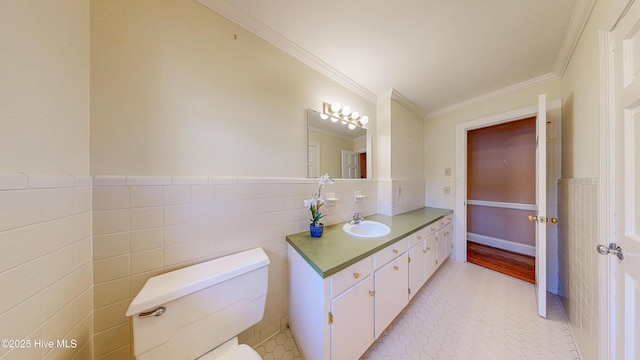 bathroom with toilet, vanity, tile walls, ornamental molding, and wainscoting