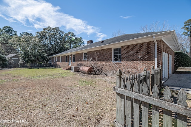 view of property exterior with brick siding, a chimney, a lawn, fence, and a garage