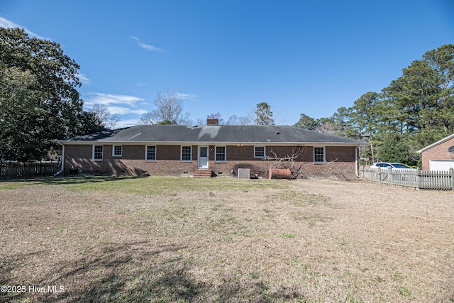 back of house with entry steps, a chimney, fence, a yard, and brick siding