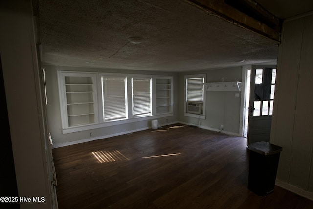 empty room featuring baseboards, dark wood-style floors, cooling unit, a textured ceiling, and built in shelves