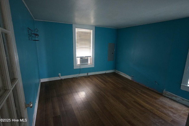 empty room with cooling unit, electric panel, baseboards, and wood finished floors