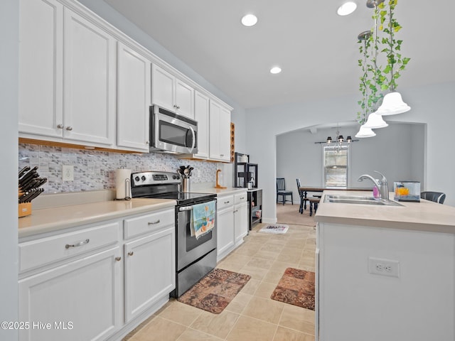 kitchen with a sink, stainless steel appliances, light countertops, white cabinets, and backsplash