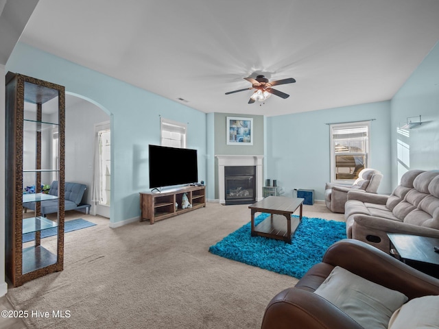 living room featuring baseboards, carpet flooring, arched walkways, a glass covered fireplace, and a ceiling fan