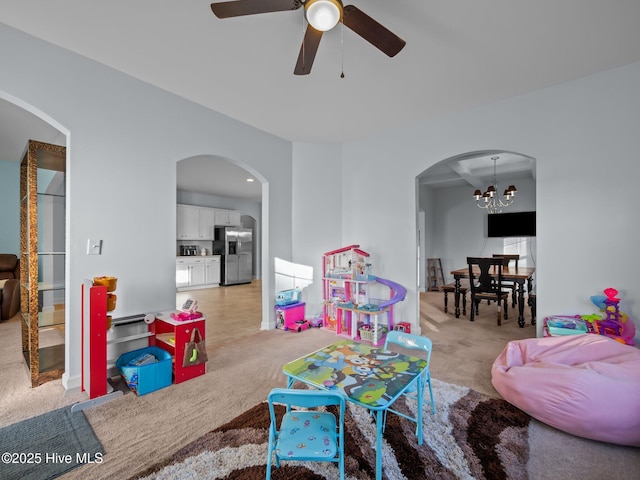 playroom featuring ceiling fan with notable chandelier, light colored carpet, and arched walkways