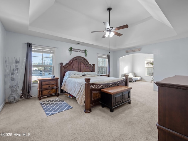 bedroom featuring multiple windows, a raised ceiling, light colored carpet, and arched walkways