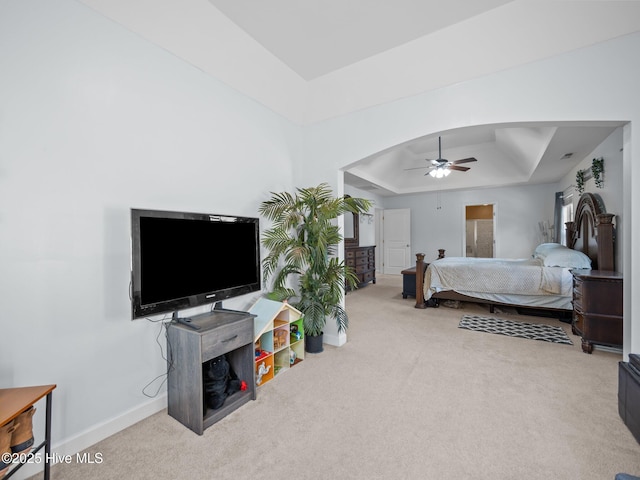 carpeted bedroom with arched walkways, a ceiling fan, a raised ceiling, and baseboards