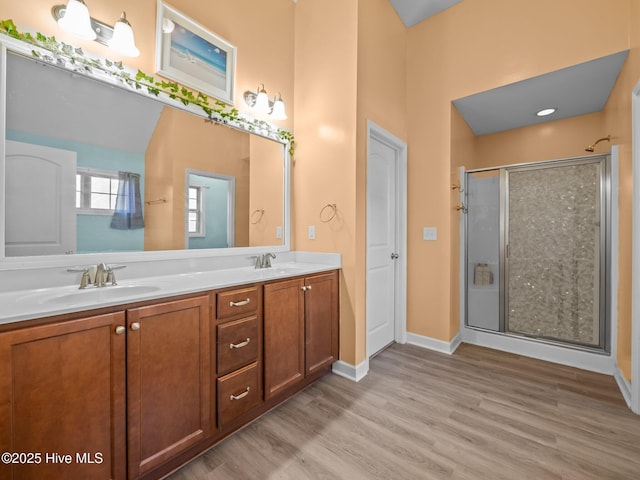 full bath with double vanity, wood finished floors, a stall shower, and a sink