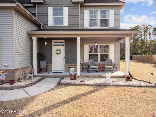 view of exterior entry featuring a yard, a porch, and fence