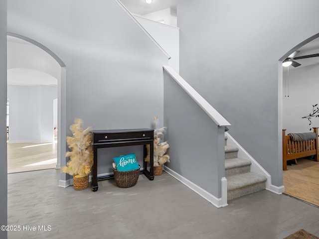 staircase with baseboards, arched walkways, ceiling fan, and a towering ceiling