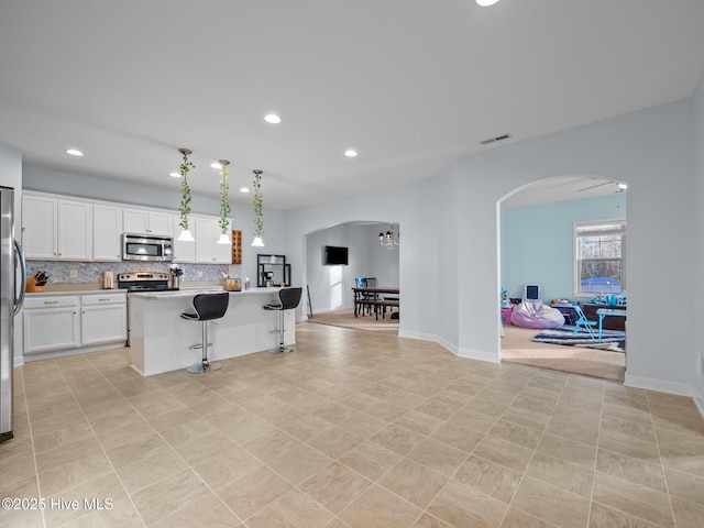 kitchen featuring arched walkways, backsplash, appliances with stainless steel finishes, and white cabinetry