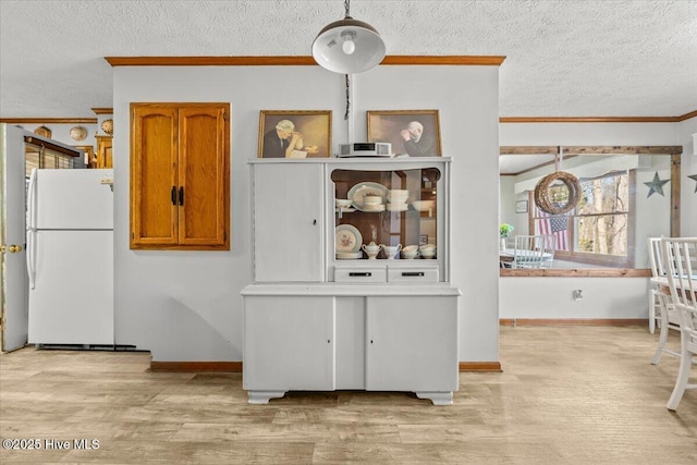 kitchen featuring light wood finished floors, ornamental molding, freestanding refrigerator, brown cabinetry, and a textured ceiling