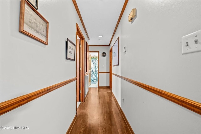 hallway featuring baseboards, ornamental molding, and wood finished floors