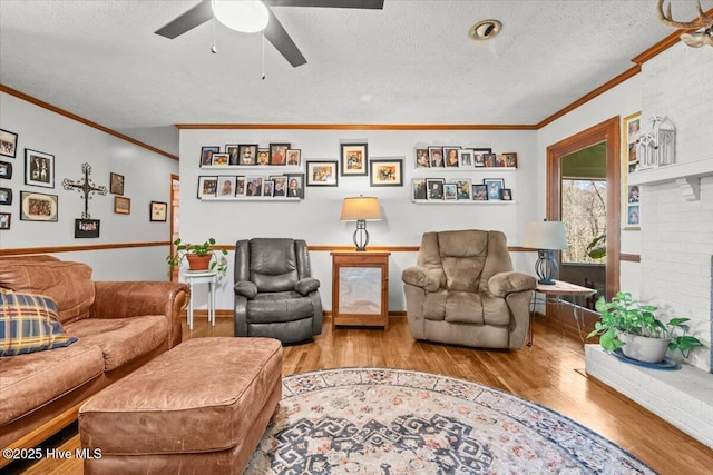 living room featuring ornamental molding, a brick fireplace, ceiling fan, a textured ceiling, and wood finished floors