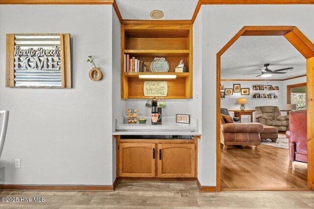 bar featuring baseboards, ornamental molding, ceiling fan, a textured ceiling, and light wood finished floors