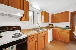 kitchen with electric range, under cabinet range hood, a sink, white dishwasher, and lofted ceiling