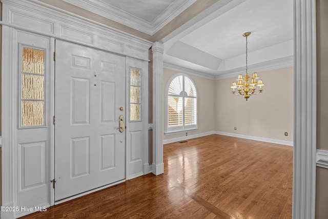 entryway featuring crown molding, a notable chandelier, ornate columns, wood finished floors, and baseboards