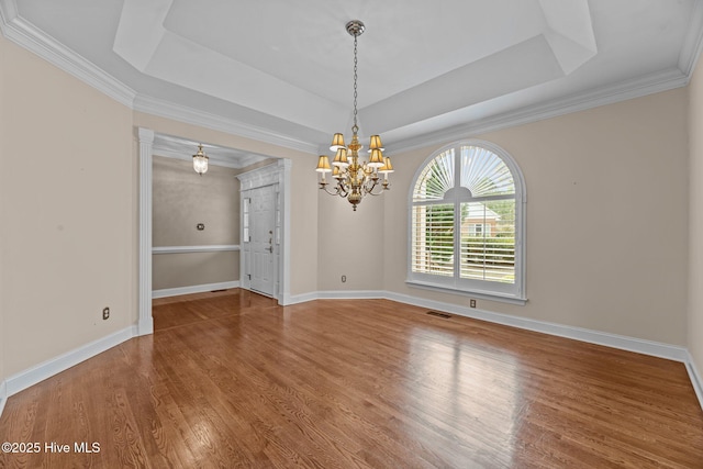 unfurnished dining area with a tray ceiling, visible vents, baseboards, and wood finished floors