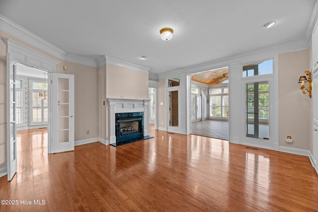 unfurnished living room featuring french doors, a premium fireplace, ornamental molding, wood finished floors, and baseboards