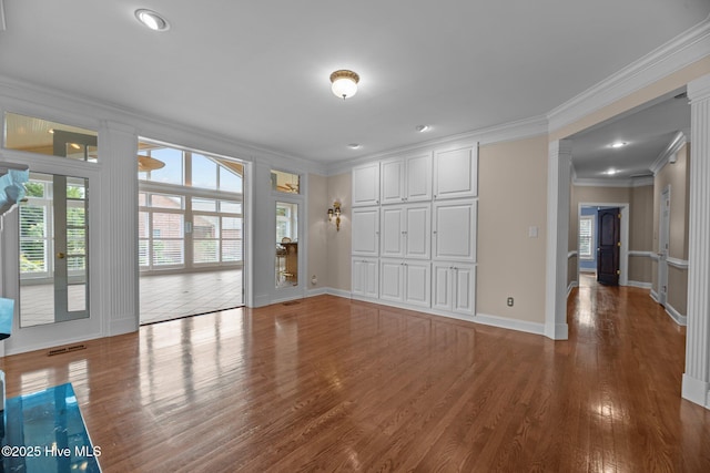 interior space featuring wood finished floors, visible vents, baseboards, ornamental molding, and decorative columns