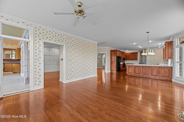 unfurnished living room featuring ceiling fan with notable chandelier, ornamental molding, light wood-style floors, and wallpapered walls