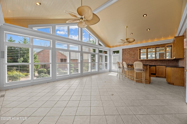 unfurnished sunroom with vaulted ceiling, a healthy amount of sunlight, ceiling fan, and a bar