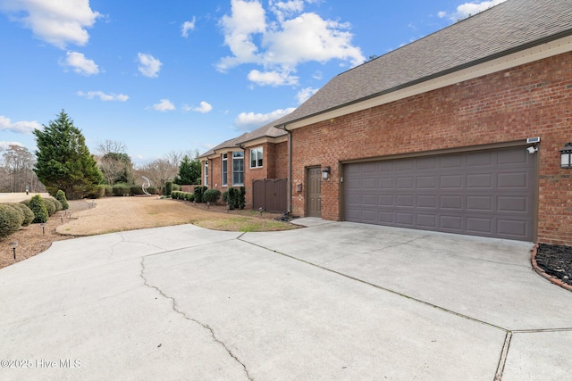 view of home's exterior with an attached garage, a shingled roof, concrete driveway, and brick siding