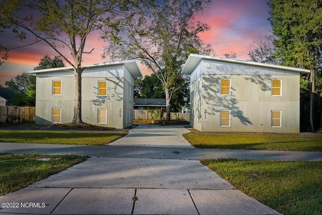 property exterior at dusk featuring fence, concrete driveway, and a yard