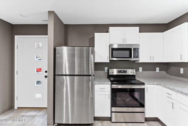 kitchen with light stone countertops, white cabinetry, appliances with stainless steel finishes, and light wood-style floors
