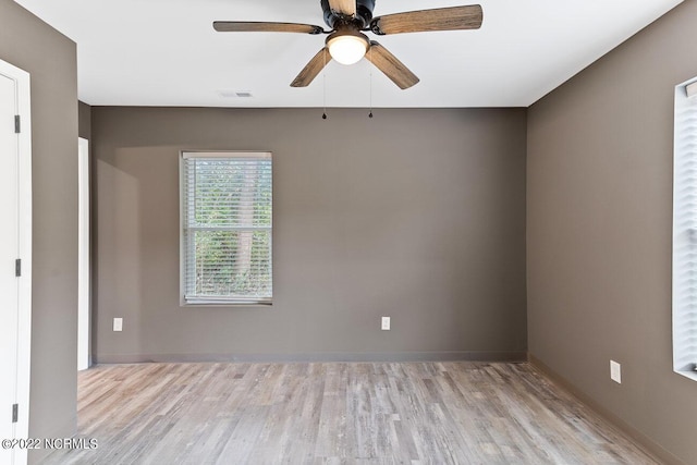 empty room featuring a ceiling fan, visible vents, baseboards, and wood finished floors