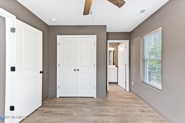 unfurnished bedroom featuring a closet, visible vents, light wood-style floors, ceiling fan, and ensuite bath