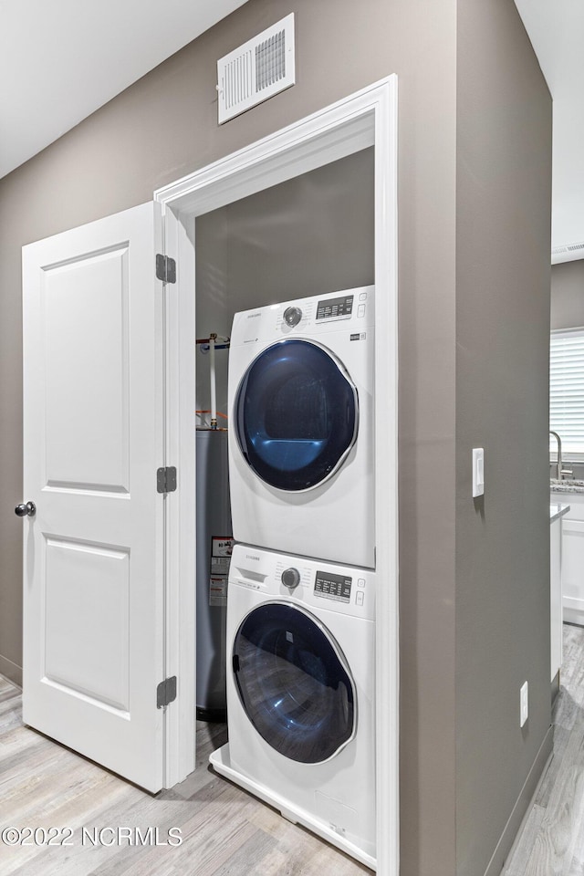 laundry room featuring laundry area, visible vents, stacked washer / dryer, and wood finished floors