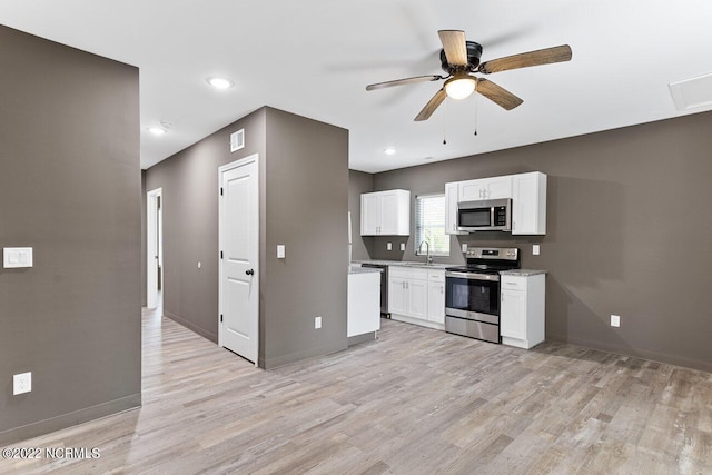 kitchen featuring stainless steel appliances, white cabinets, a sink, light wood-type flooring, and baseboards