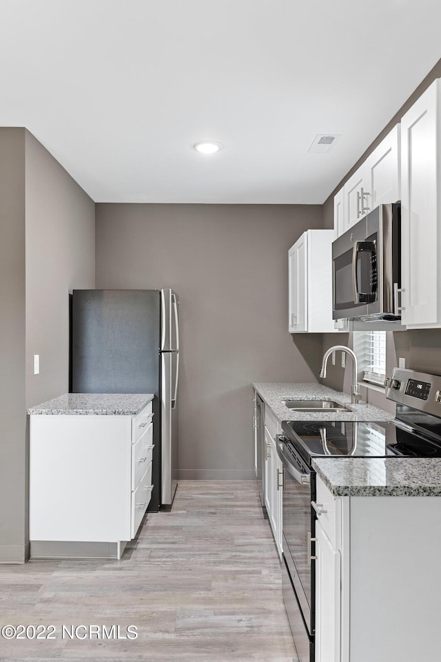 kitchen with light stone countertops, white cabinetry, appliances with stainless steel finishes, and a sink
