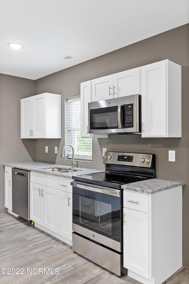 kitchen with light wood-style flooring, stainless steel appliances, a sink, white cabinets, and light stone countertops