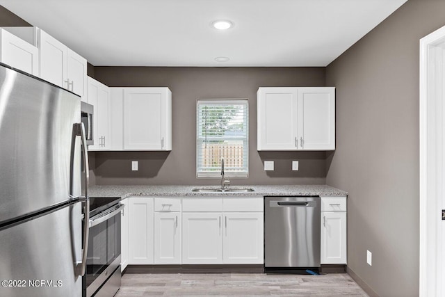 kitchen featuring light wood-style flooring, light stone countertops, stainless steel appliances, white cabinetry, and a sink