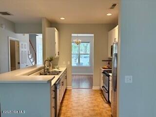 kitchen with electric stove, light countertops, white cabinets, a sink, and baseboards