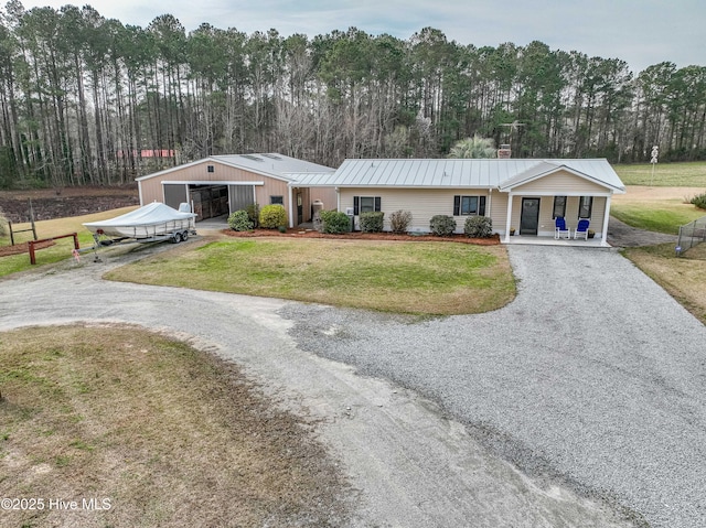 view of front of property with gravel driveway, a front lawn, an outdoor structure, a garage, and metal roof