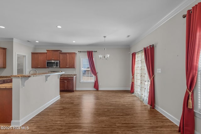 kitchen with ornamental molding, stainless steel microwave, a breakfast bar, dark wood-type flooring, and a chandelier