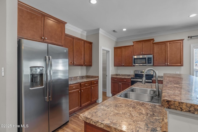 kitchen featuring recessed lighting, stainless steel appliances, a sink, ornamental molding, and light wood finished floors