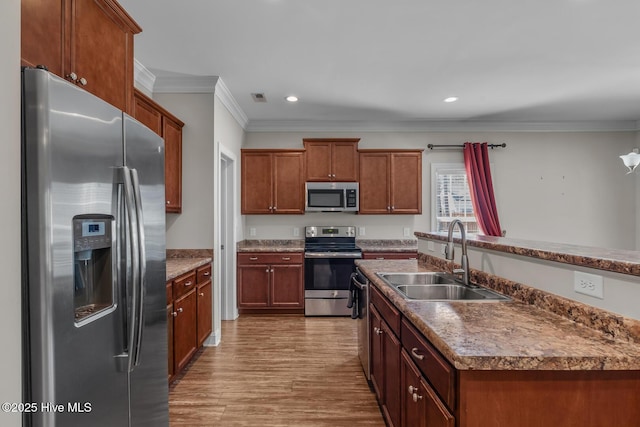 kitchen featuring visible vents, appliances with stainless steel finishes, ornamental molding, wood finished floors, and a sink