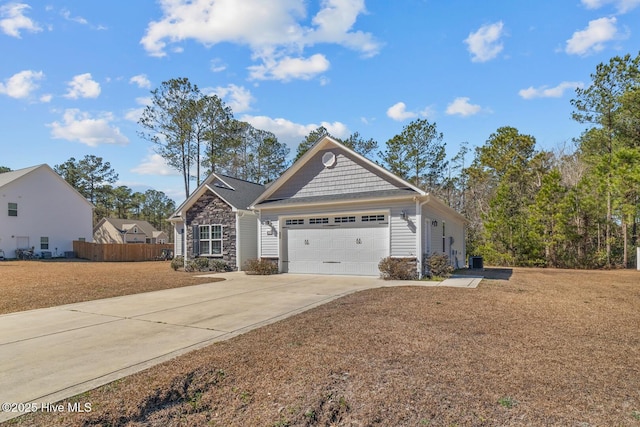 view of front facade with a garage, stone siding, driveway, and fence